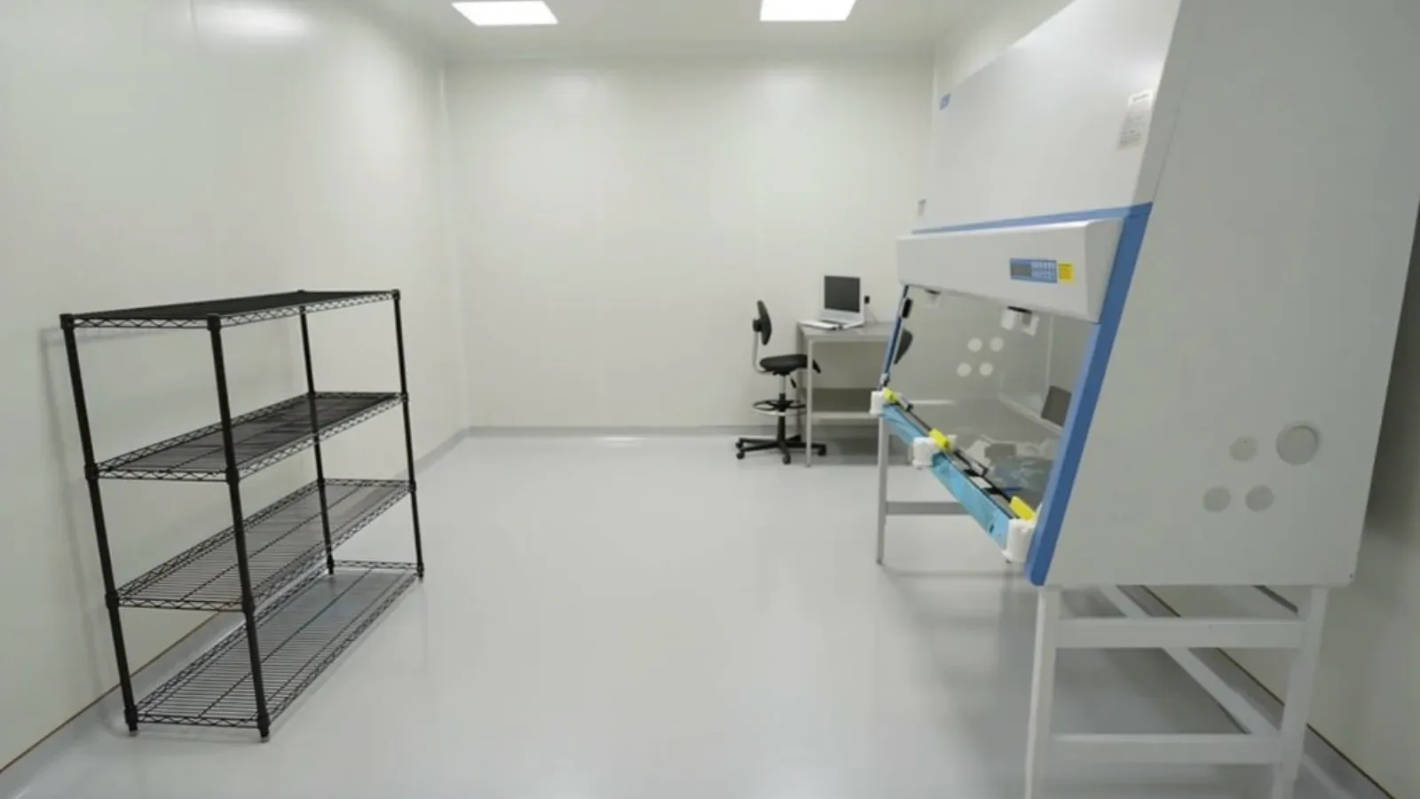 A cleanroom corridor with seamless sealed white wall panels, a coved floor and lab equipment along one side